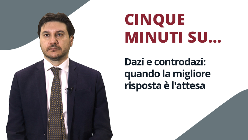 Un uomo in giacca e cravatta parla con accanto un testo che recita: "CINQUE MINUTI SU... Dazi e controdazi: quando la migliore risposta è l'attesa", trasmettendo un tono riflessivo.