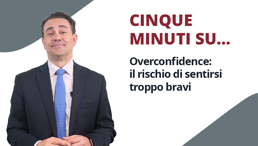 Uomo in giacca e cravatta con espressione felice in piedi accanto al testo: “CINQUE MINUTI SU... Overconfidence: il rischio di sentirsi troppo bravi" su sfondo bianco e grigio.