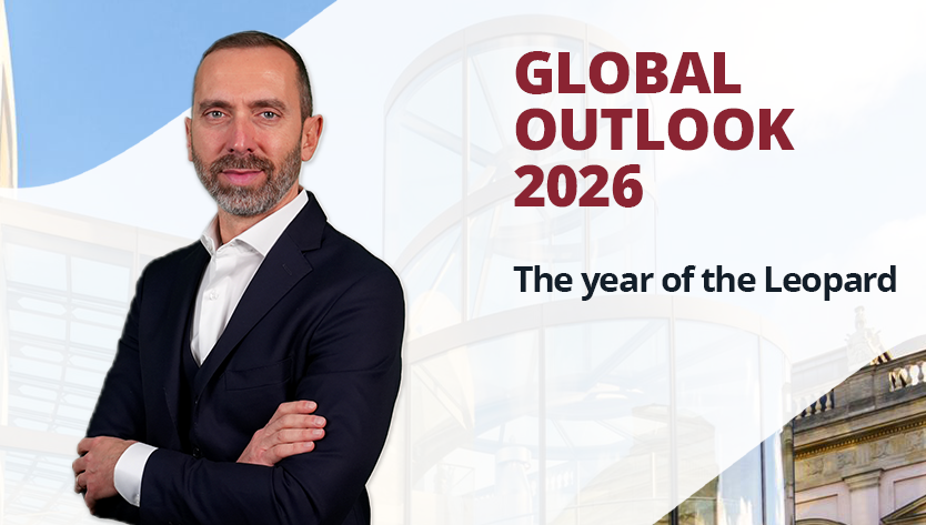 Un uomo sicuro di sé in abito scuro sta in piedi a braccia conserte, sorridendo. Lo sfondo presenta un'architettura moderna e la scritta “Global Outlook 2026”.