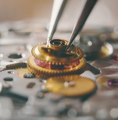 Primo piano di un orologiaio che inserisce un piccolo ingranaggio dorato nel meccanismo di un orologio usando delle pinzette.