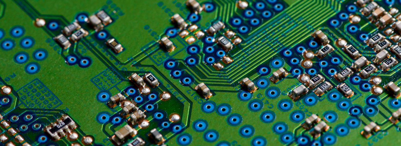 Primo piano di una scheda a circuito stampato verde, con punti di saldatura blu e vari piccoli componenti elettronici.