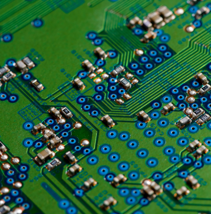 Primo piano di una scheda a circuito stampato verde, con punti di saldatura blu e vari piccoli componenti elettronici.