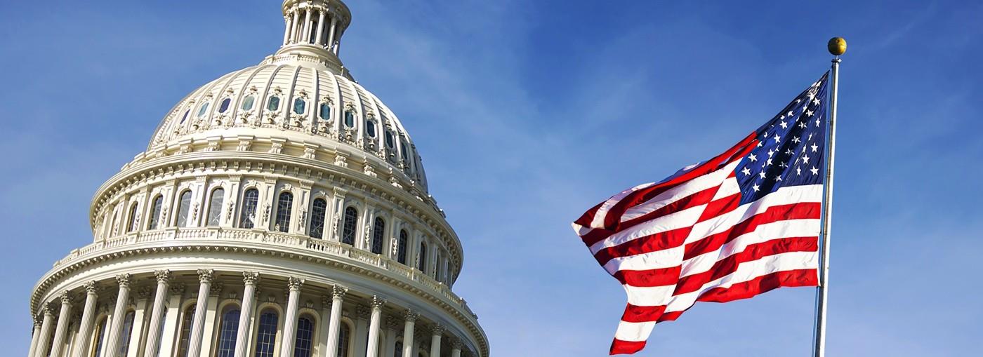 La cupola del Campidoglio degli Stati Uniti svetta sopra una bandiera americana sventolante, sotto un cielo azzurro e limpido.
