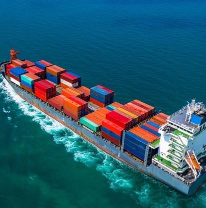 Veduta aerea di una grande nave cargo carica di container colorati che naviga attraverso acque oceaniche blu.