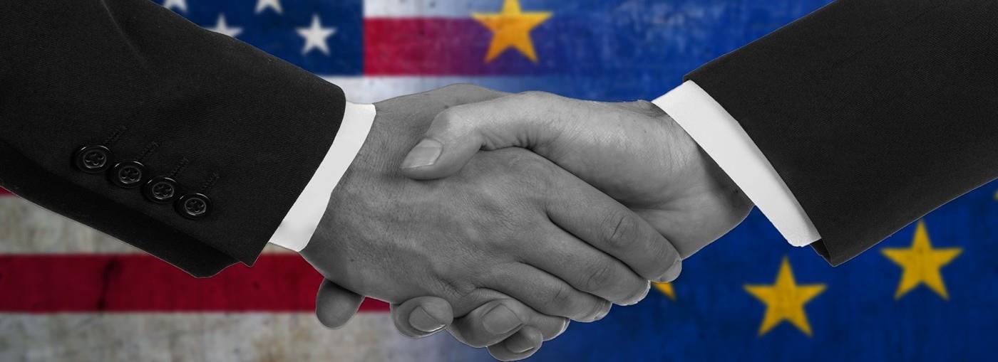 Due mani che si stringono su uno sfondo con le bandiere degli Stati Uniti e dell&#39;Unione Europea