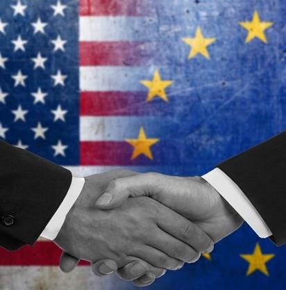 Due mani che si stringono su uno sfondo con le bandiere degli Stati Uniti e dell&#39;Unione Europea