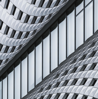 Close-up of a modern building facade with geometric, metallic patterns and tall vertical glass windows reflecting light.