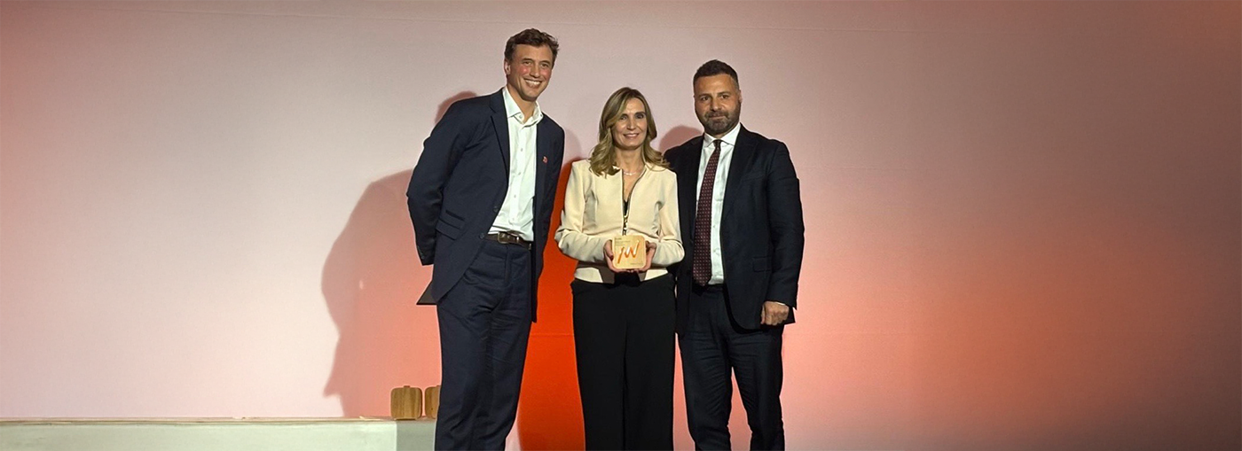 Tre persone sono in piedi sul palco, con in mano un premio, davanti a uno sfondo sfumato illuminato.