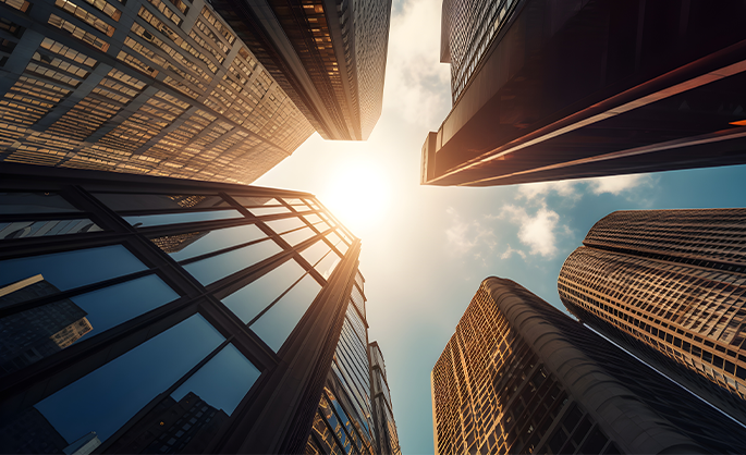 Upward view of tall skyscrapers against a bright sky, sun shining through, reflecting on glass facades, creating a vibrant, urban atmosphere.